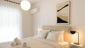 Una habitación de hotel moderna con una cama bien hecha, una lámpara de noche y un aire acondicionado instalado en la pared.