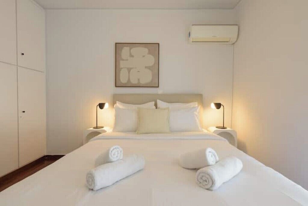 Habitación de hotel con cama, dos lámparas de noche, aire acondicionado de pared y una obra de arte enmarcada sobre la cama.