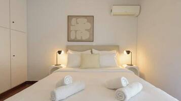 Habitación de hotel con cama, dos lámparas de noche, aire acondicionado de pared y una obra de arte enmarcada sobre la cama.