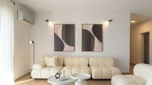 Una sala moderna con un sofá color beige, dos mesitas blancas y arte abstracto en la pared.