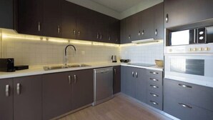 Una cocina moderna con armarios oscuros, un lavavajillas de acero inoxidable, una encimera blanca y un horno empotrado.
