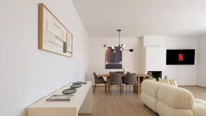 Una sala de estar moderna con un sofá, una mesa de comedor, sillas, un televisor y un cuadro en la pared.