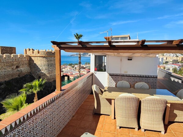 Une terrasse avec une table et des chaises, une vue sur un ancien mur de pierre et un ciel bleu dégagé.