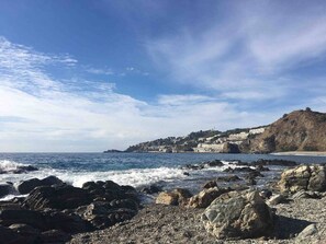 A rocky shoreline with waves, a clear sky, and a distant hill with buildings. - Maison Almuñecar centre ! vue mer château montagne (Almuñécar)