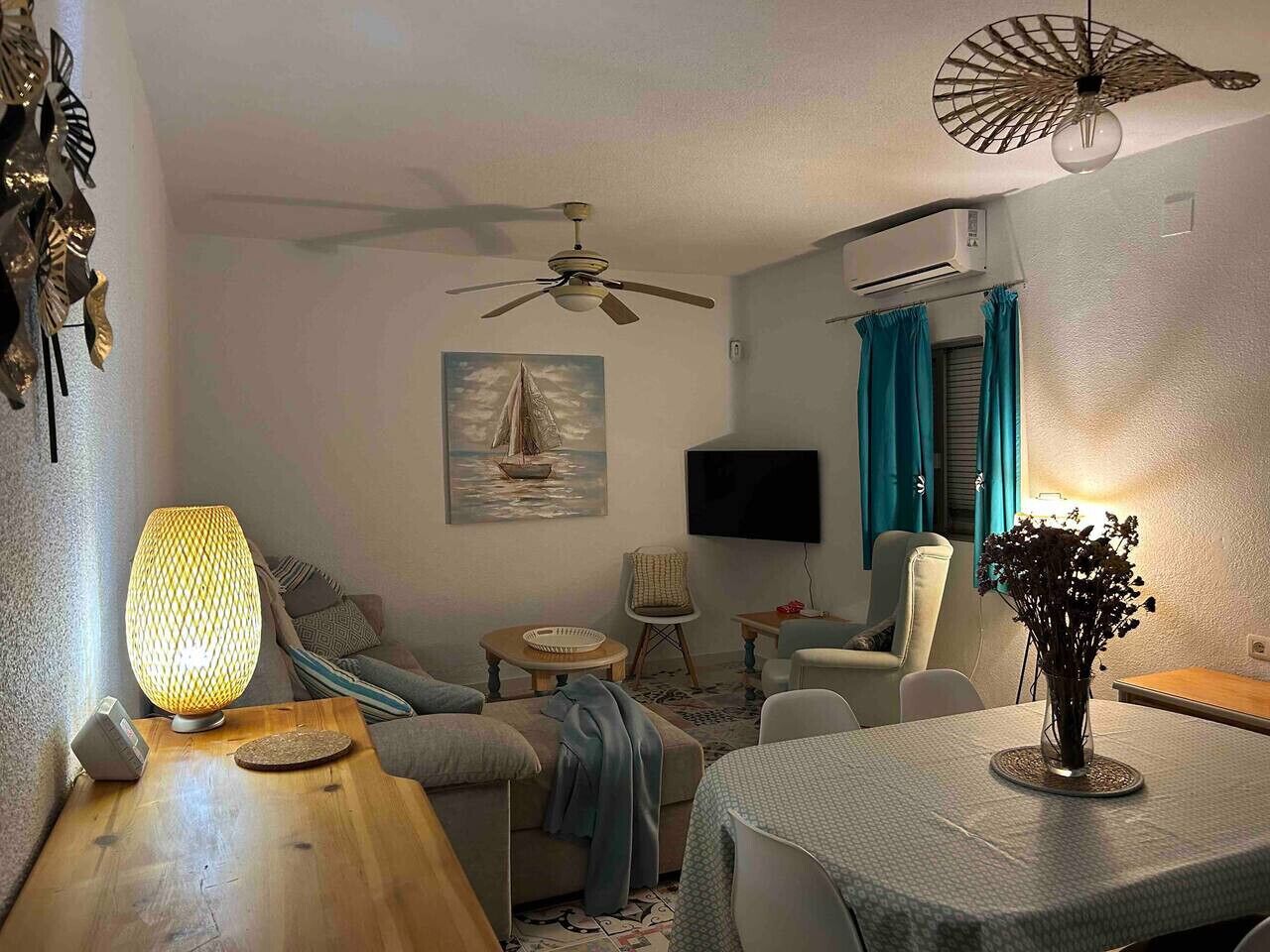 A living room with a sofa, a table, a TV, a ceiling fan, and a window with curtains.