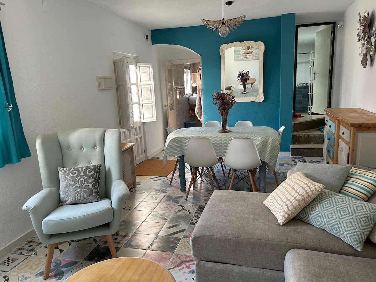 Uma sala de estar com sofá, poltrona, mesa de jantar, cadeiras e um armário.