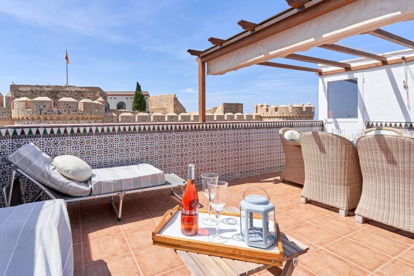 Eine Dachterrasse mit Tisch, Liegestühlen und Blick auf historische Gebäude.