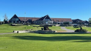 Campo de golf con club de campo que cuenta con varios edificios, senderos de piedra y césped bien cuidado.