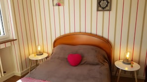 A bedroom with a wooden headboard, a heart-shaped pillow, and two bedside tables with lamps.