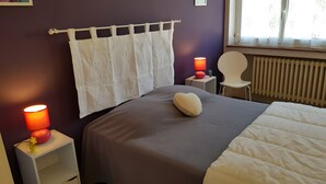 A bedroom with a bed, a nightstand with a lamp, a chair, and a window with curtains.