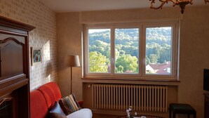 A room with a red sofa, a radiator, and a window with a view of trees and houses.
