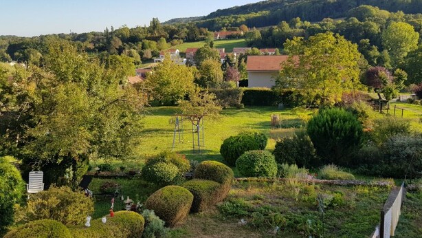 A lush garden with neatly trimmed hedges, a playground, and a view of a village in the background.