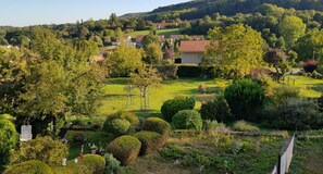 A lush garden with neatly trimmed hedges, a playground, and a view of a village in the background.