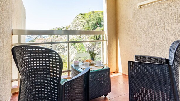 En balkon med to fletstole, et lille bord med kop og underkop, og en potteplante.
