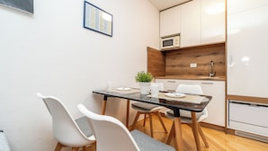 Een compacte keuken met een magnetron, houten kastjes en een kleine eethoek met twee stoelen en een tafel.