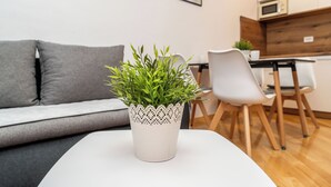 Een moderne woonkamer met een grijze bank, een witte tafel met een potplant en een eethoek van hout.