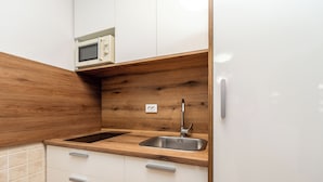 Een keuken met houten kastjes, een roestvrijstalen spoelbak, een magnetron en een witte koelkast.