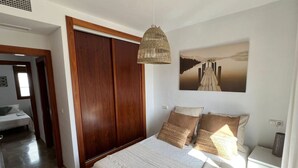 A bedroom with a bed, a wooden wardrobe, a hanging light fixture, and a painting on the wall.