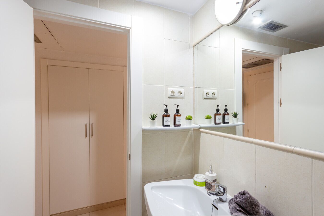 Un bagno con un lavandino bianco, uno specchio e uno scaffale con articoli da toilette.