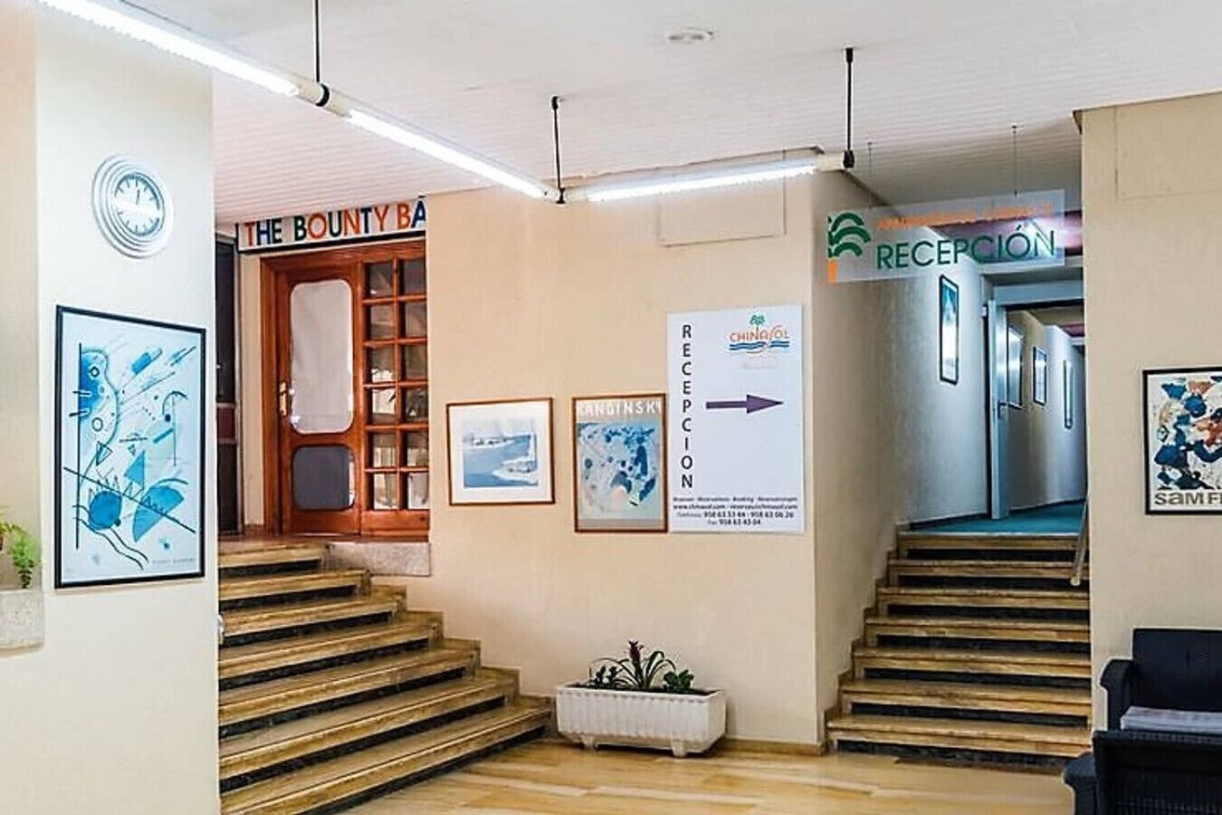 Uma área de recepção com um letreiro de 'The County Bank', um balcão de atendimento e uma escadaria que leva a outro andar.