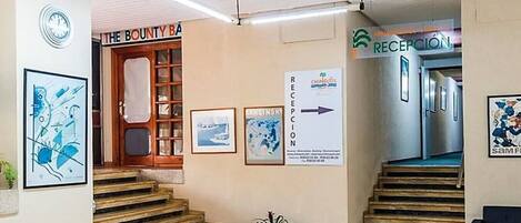 Uma área de recepção com um letreiro de 'The County Bank', um balcão de atendimento e uma escadaria que leva a outro andar.