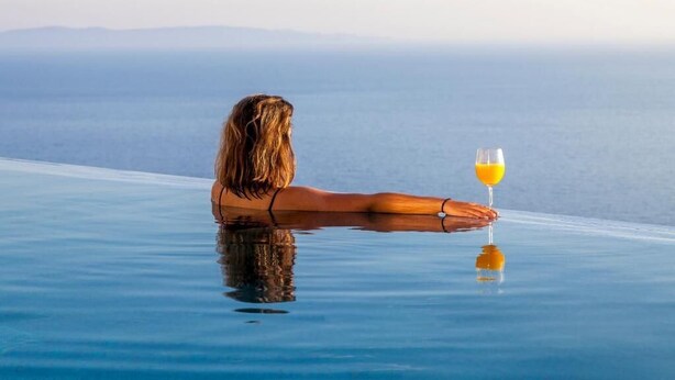 Une personne se détend au bord d’une piscine à débordement en verre, un verre de jus d’orange à la main.