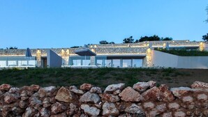 Un bâtiment moderne avec des murs en pierre, de grandes fenêtres et des espaces extérieurs aménagés pour s’asseoir.