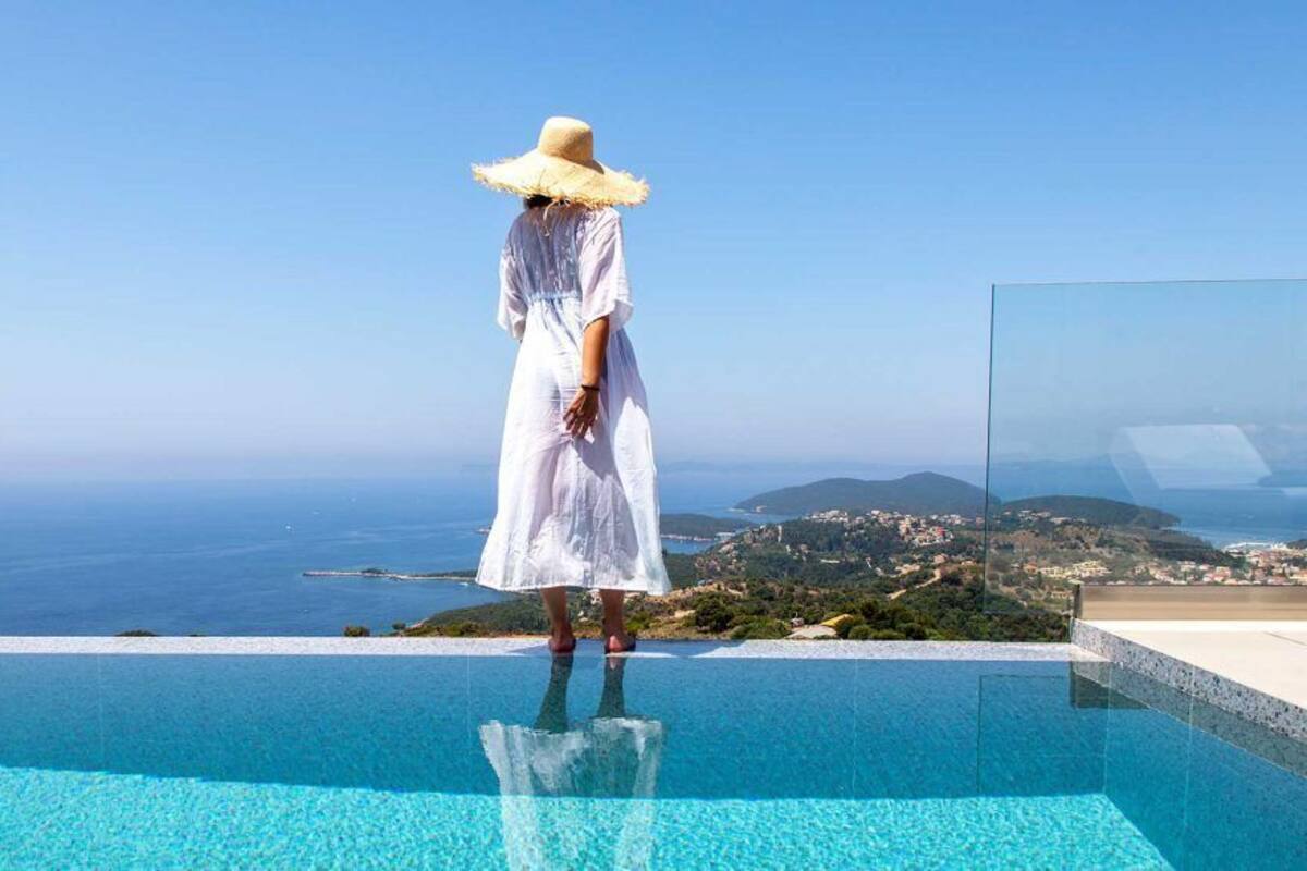 Eine Person steht am Rand eines Infinity-Pools mit Blick auf das Meer und die ferne Landschaft.