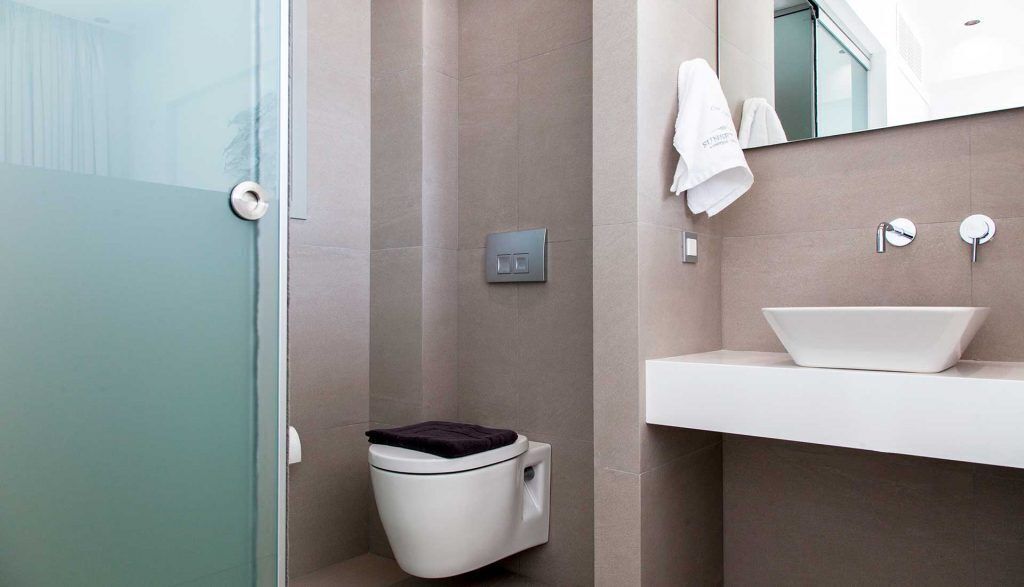 A modern bathroom with a glass shower enclosure, a toilet with a dark lid, a white sink with a vessel basin, and a towel hanging on the wall.