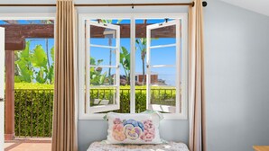 Ein Zimmer mit großem Fenster, einer gepolsterten Bank und Blick auf Grünflächen und ein Gebäude.