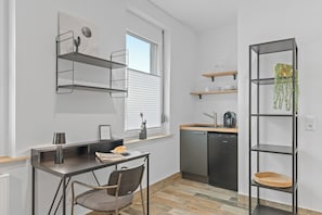 A compact kitchen with a dining area, built-in shelves, and a window with blinds. - RICLS Apartmenthaus - BRIGHT Collection (Wurmberg)