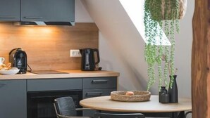 A modern kitchen with grey cabinets, a round wooden table, and hanging plants. - RICLS Apartmenthaus - BRIGHT Collection (Wurmberg)
