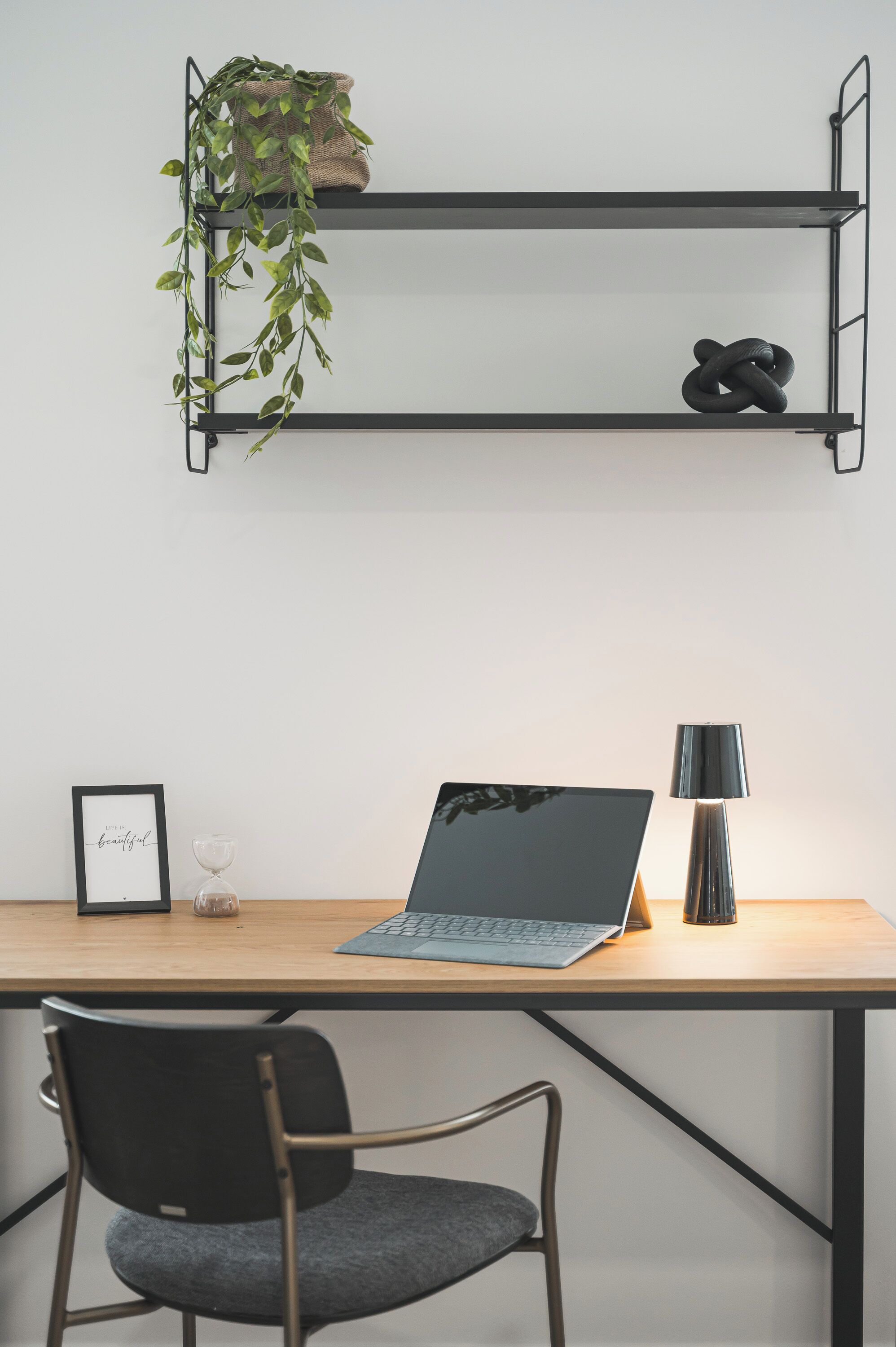 A workspace with a laptop, a lamp, a chair, and a shelf with a plant and a shoe.