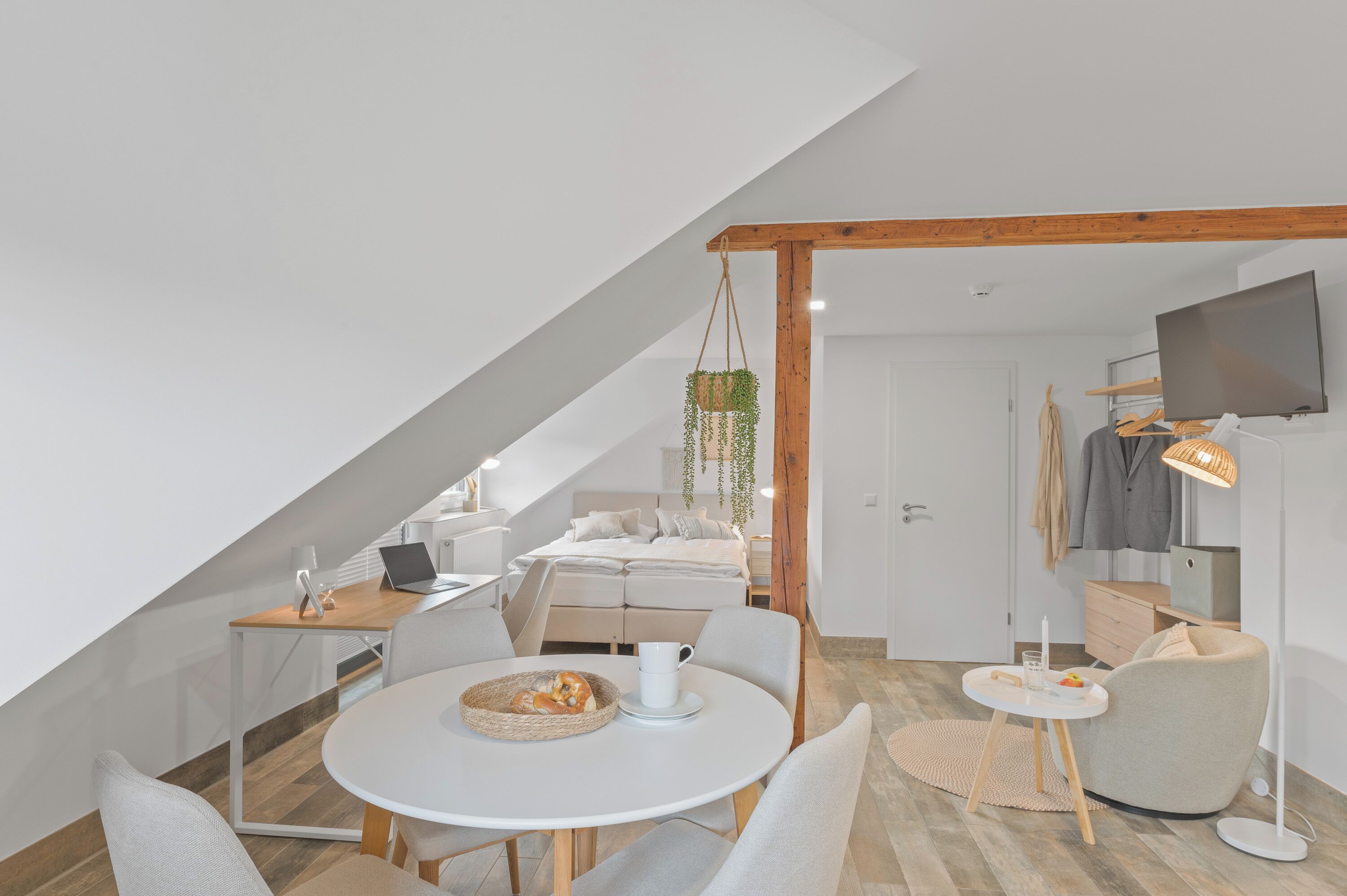 A modern loft bedroom with a sloped ceiling, a bed, a desk, and a dining area.