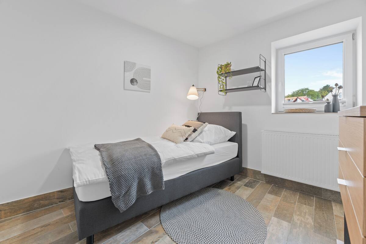 A modern bedroom with a bed, bedside lamp, and a view through a window.