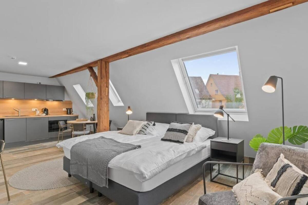 A modern loft bedroom with a large bed, a desk, and a kitchenette.