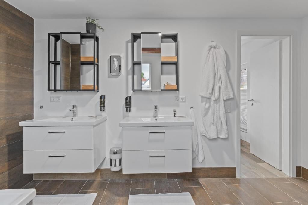 Une salle de bain moderne avec deux lavabos, un miroir, un porte-serviettes et une porte.