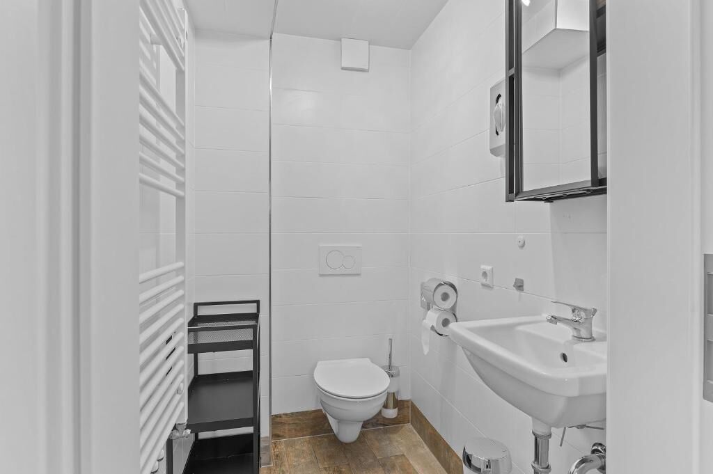 Ein kleines, modernes Badezimmer mit Toilette, Waschbecken und Spiegel.