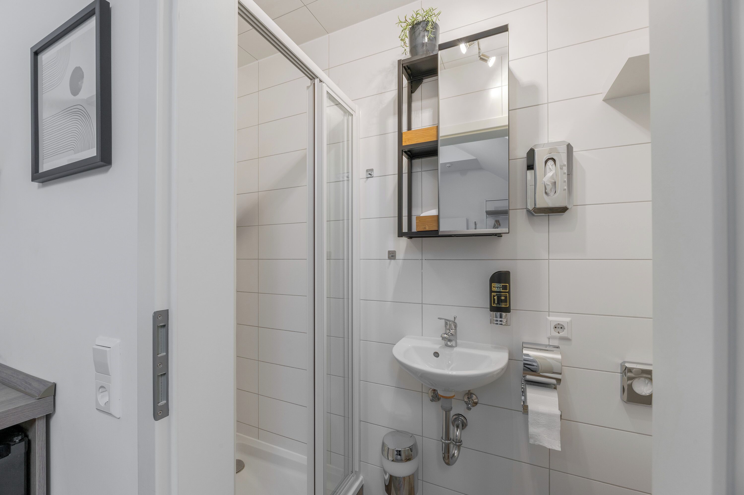 Un baño moderno con mampara de vidrio, un lavabo blanco, un espejo y dispensador de papel higiénico.