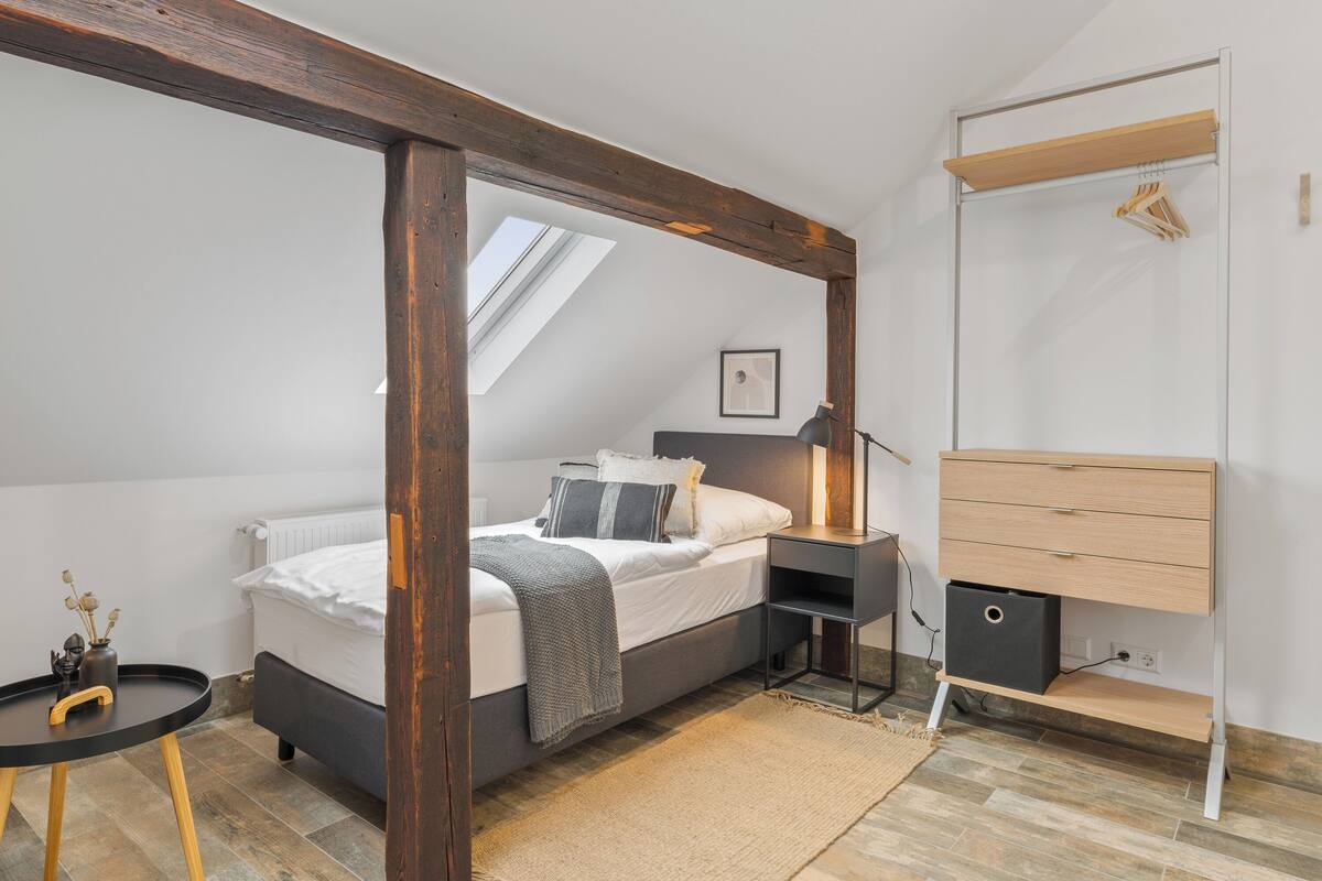 A bedroom with a bed, bedside table, lamp, and a wooden dresser.
