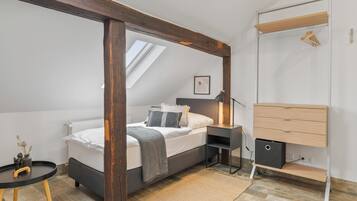 A bedroom with a bed, bedside table, lamp, and a wooden dresser.