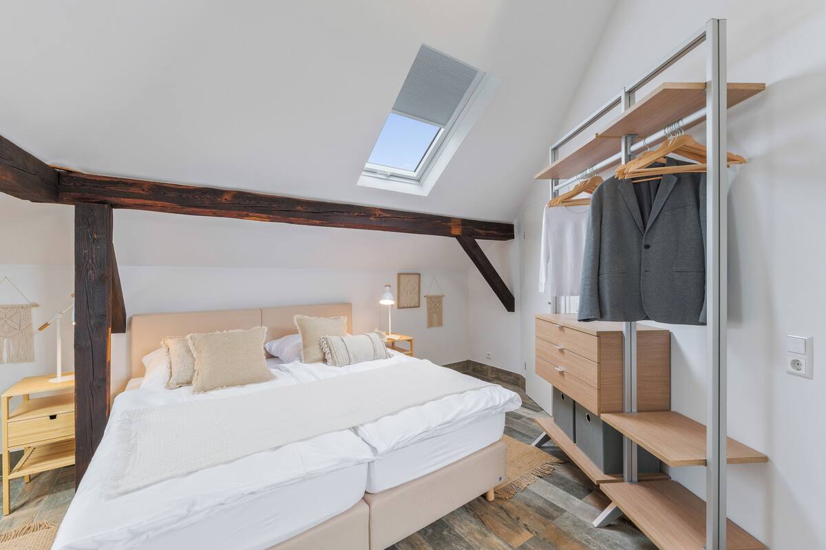 A bedroom with a skylight, a bed, a wardrobe, and a bedside table.