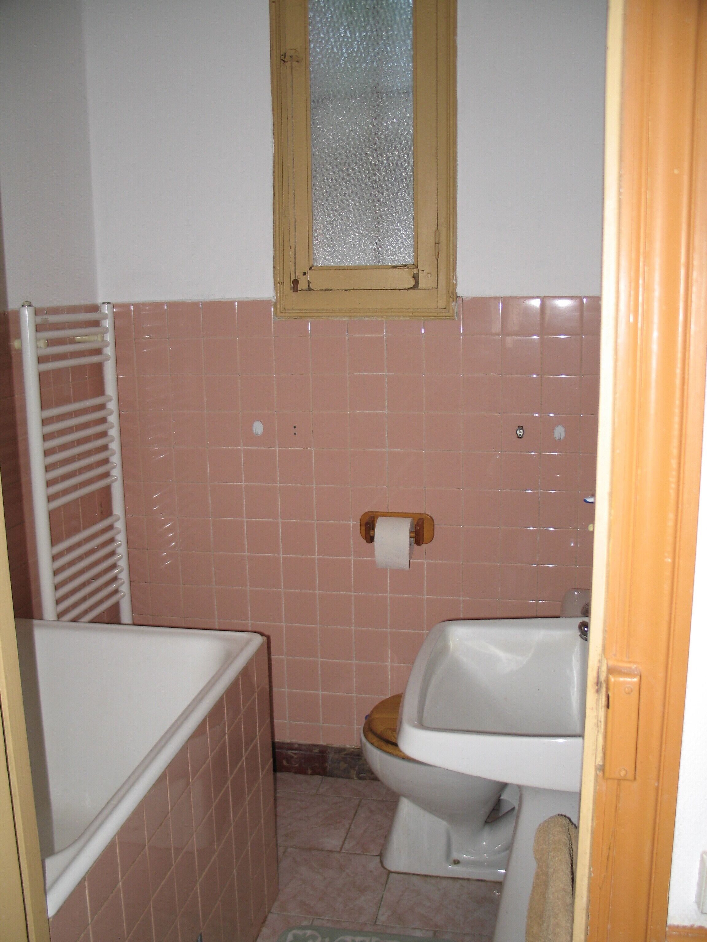 Une petite salle de bain comprenant des toilettes, un lavabo et une fenêtre avec un vitrage dépoli.