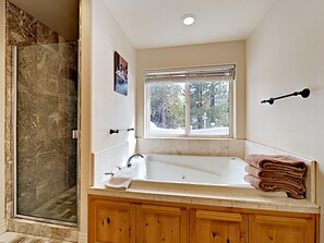 Un bagno con doccia in marmo, una vasca da bagno ampia, mobili in legno, una finestra con vista sugli alberi e un portascopevoli.