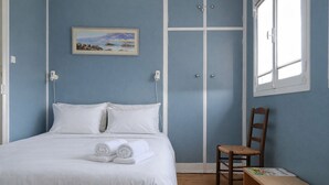 A bedroom with a bed, pillows, a chair, a bench, a picture on the wall, and a window. - Charming house near the beach for 6 people (Les Sables-d´Olonne)
