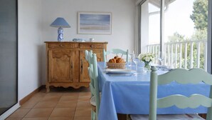 A dining area with a table set for two, a wooden cabinet, a lamp, and a painting on the wall. - Charming house near the beach for 6 people (Les Sables-d´Olonne)