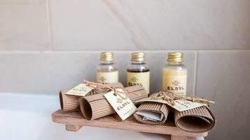 A wooden shelf with rolled-up towels and bottles of ELSYL shower cap.