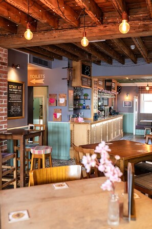 A restaurant with wooden beams, hanging light bulbs, a bar area, and a sign for toilets. - Cherry Tree Inn  (Horbury)