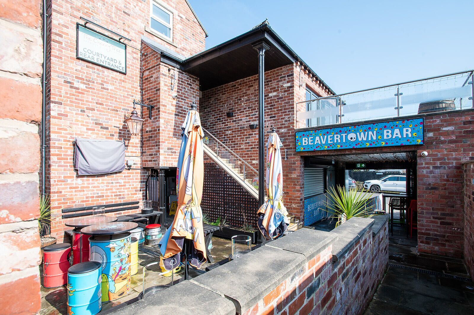 A brick building with a sign for Beaverton Bar, outdoor seating with umbrellas, and a staircase leading to the entrance.