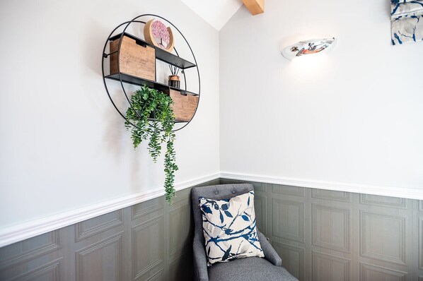 A corner with a grey upholstered chair, a wall-mounted wooden shelf with a hanging plant, and a decorative wall piece. - Cherry Tree Inn (Horbury)